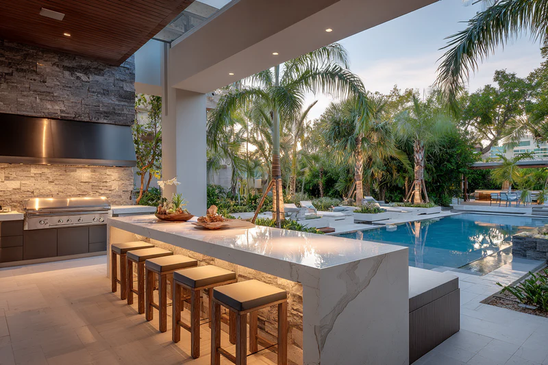Outdoor kitchen with pool and palm trees at dusk
